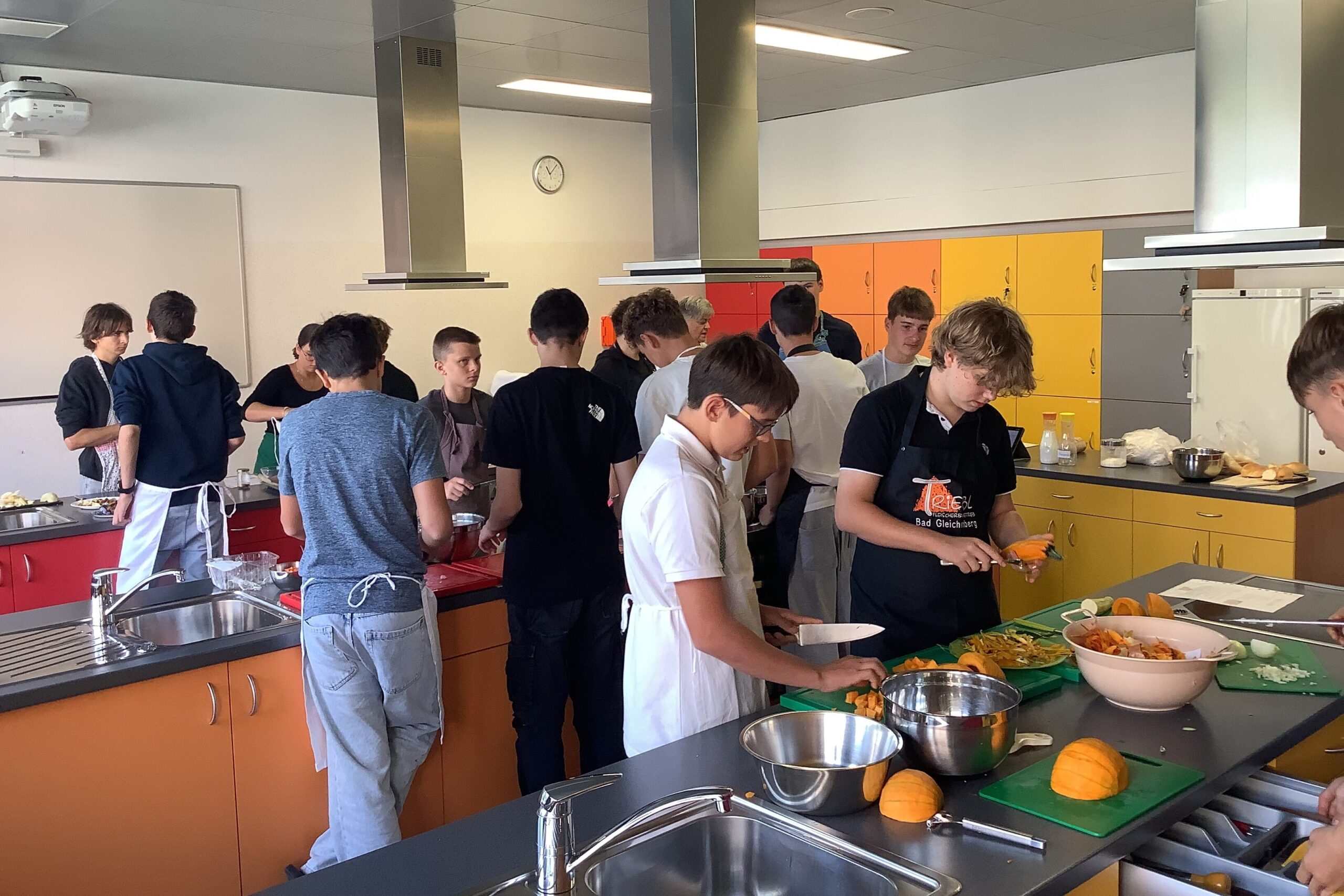 Schüler in Kochschürzen schnippeln Gemüse in einer Schulküche in Bad Gleichenberg.